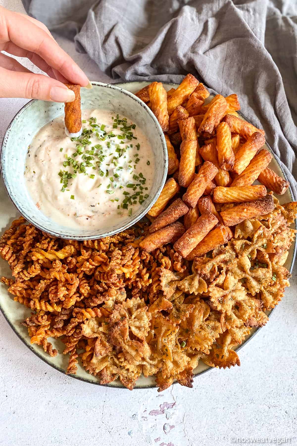 Air fryer pasta chips on plate with dipping sauce. Hand dipping pasta chip into sauce.