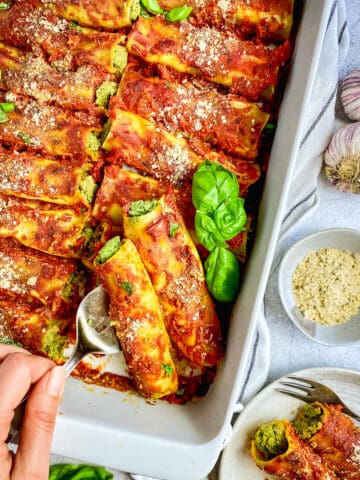 Vegan cannelloni in pan with hand serving.