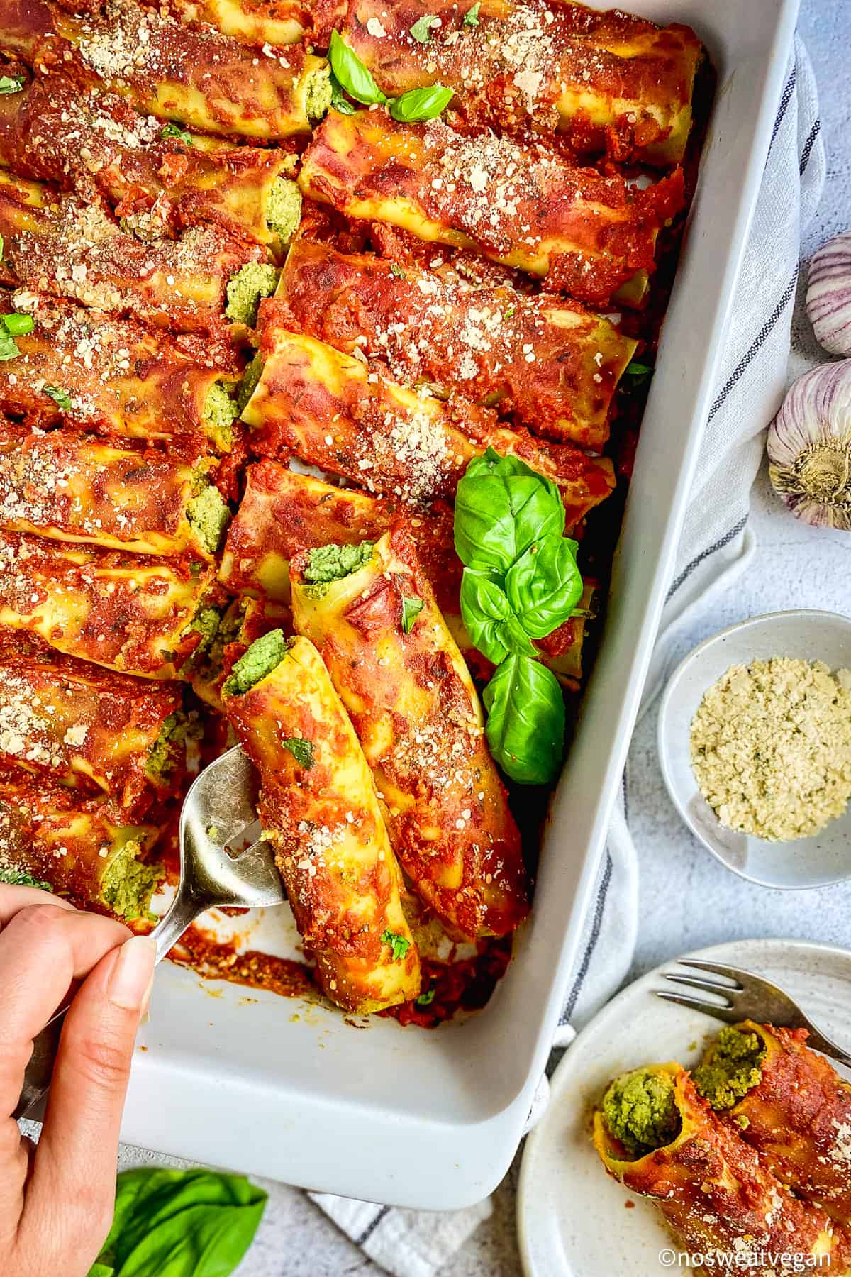 Vegan cannelloni in pan with hand serving.