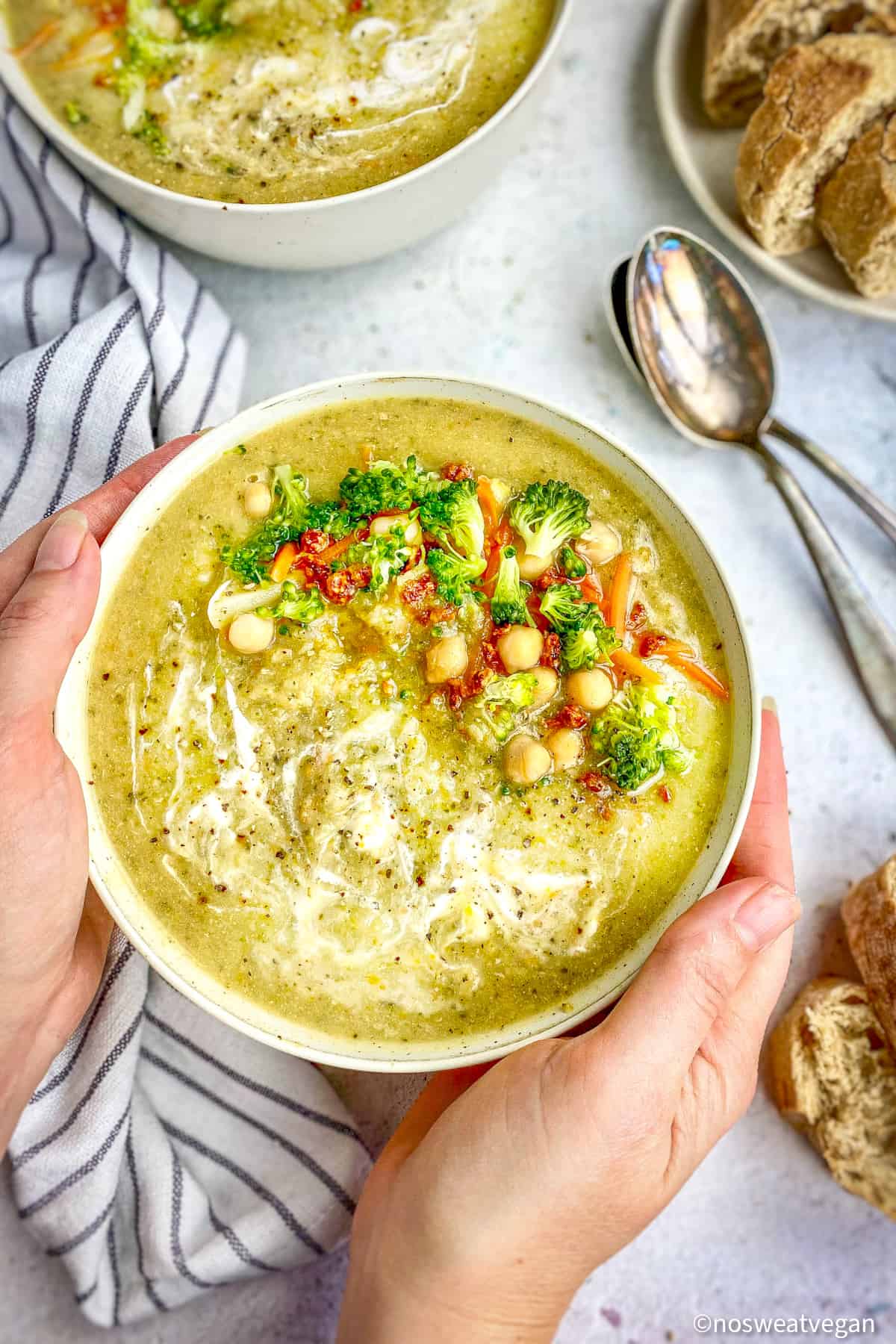 Vegan broccoli soup in a bowl with two hands holding the bowl.