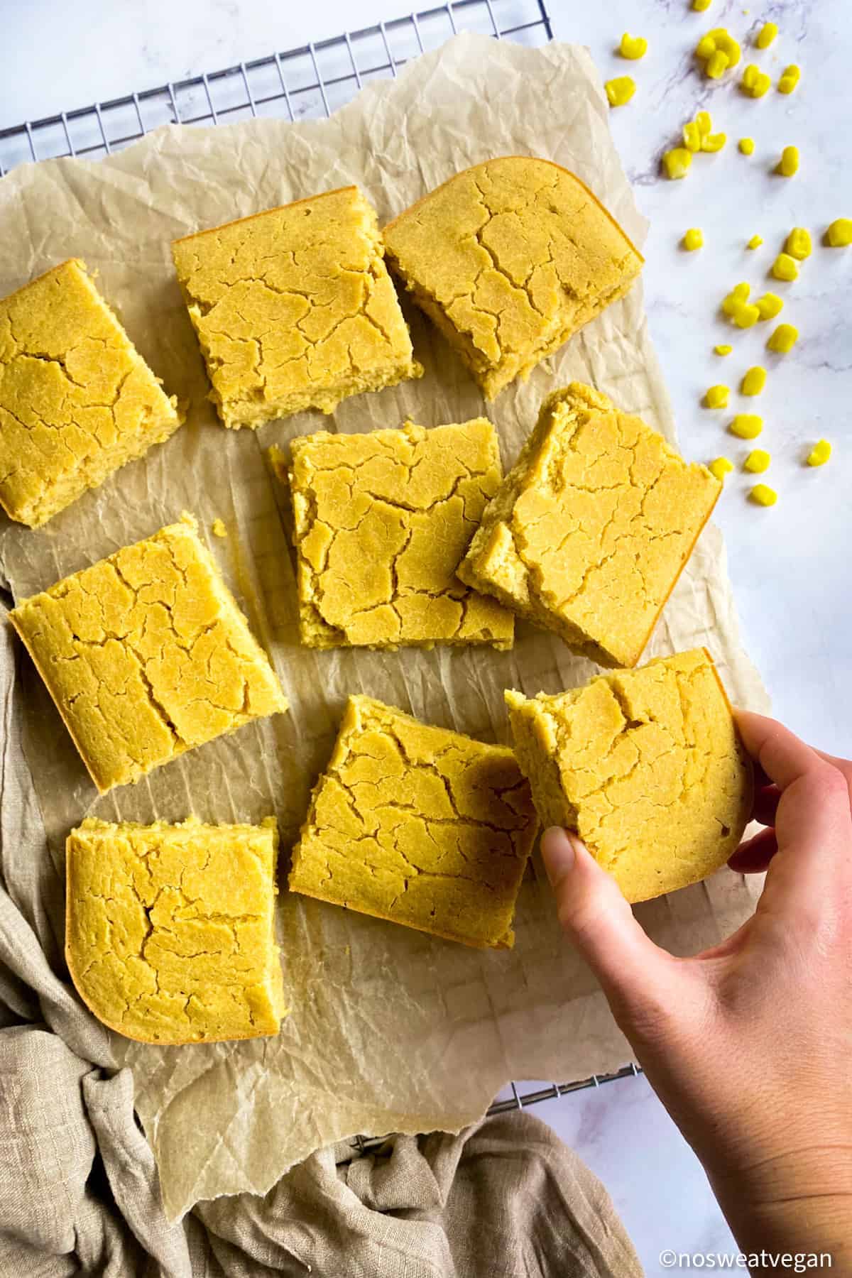 Vegan cornbread on a drying rack with hand picking up one piece.