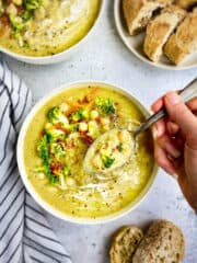 Vegan cream of broccoli soup in bowl with hand holding a spoon.