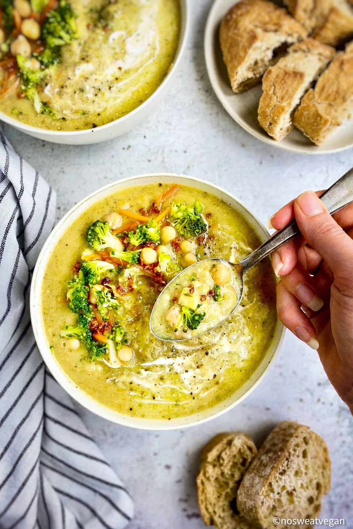 Vegan cream of broccoli soup in bowl with hand holding a spoon.