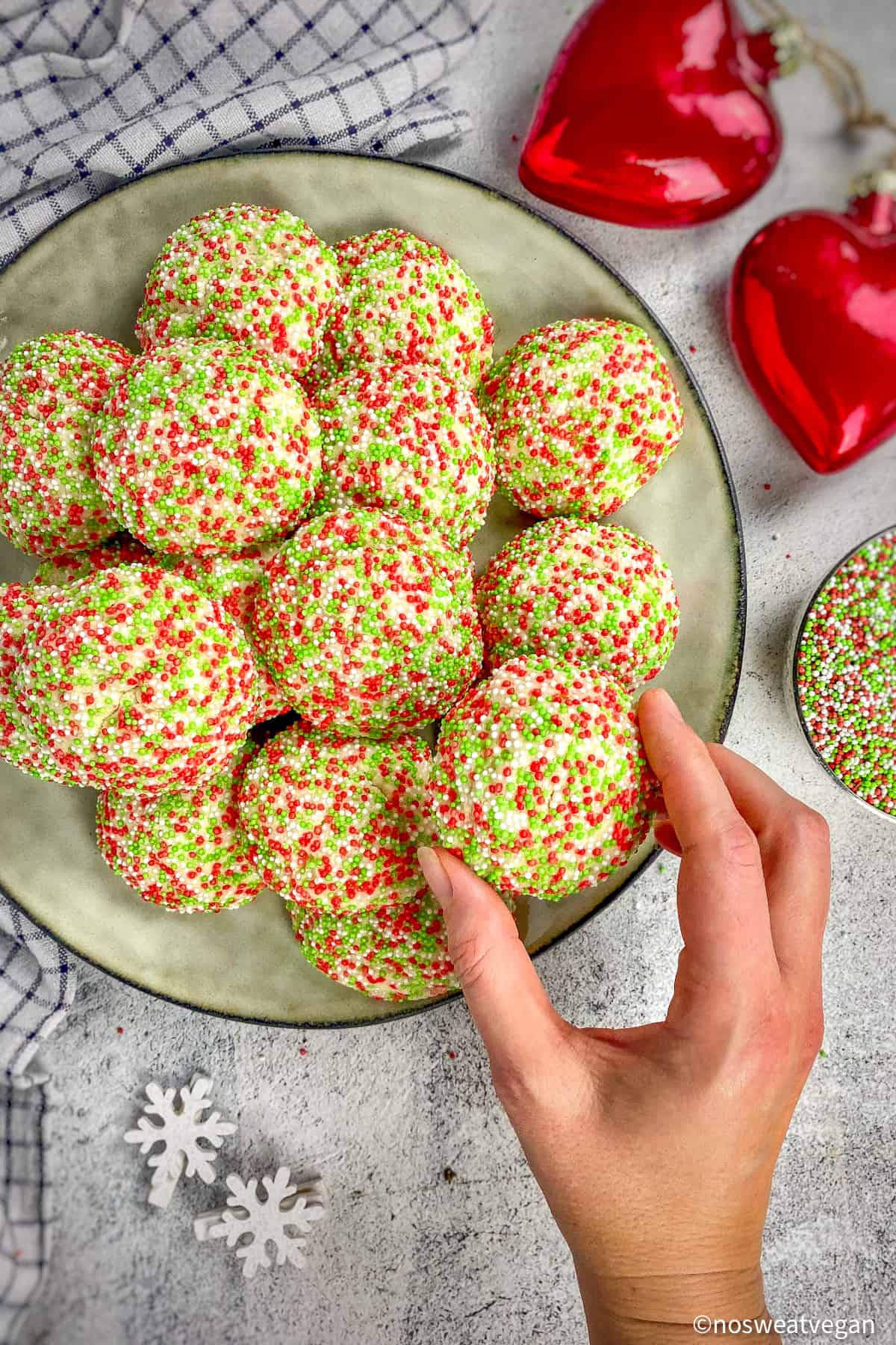 Christmas sprinkle cookies on a plate with a hand picking one up.