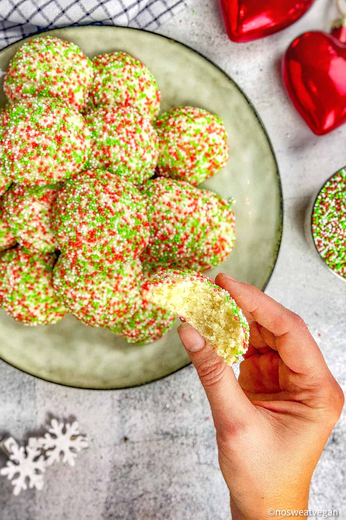 Vegan Christmas sprinkle cookies on plate with hand holding one cookie with bite taken out.