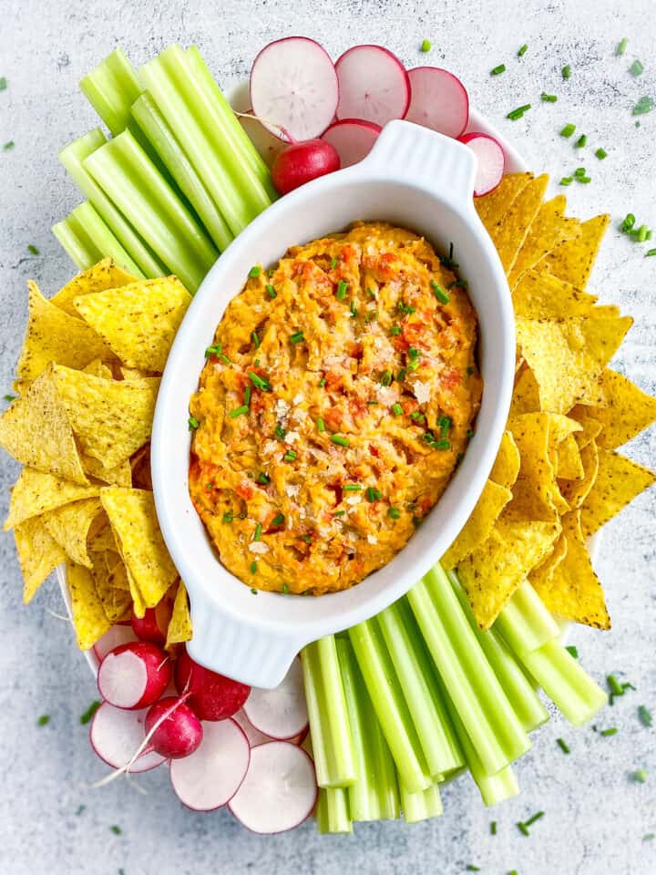 Buffalo chickpea dip on platter with chips, celery, and sliced radishes.