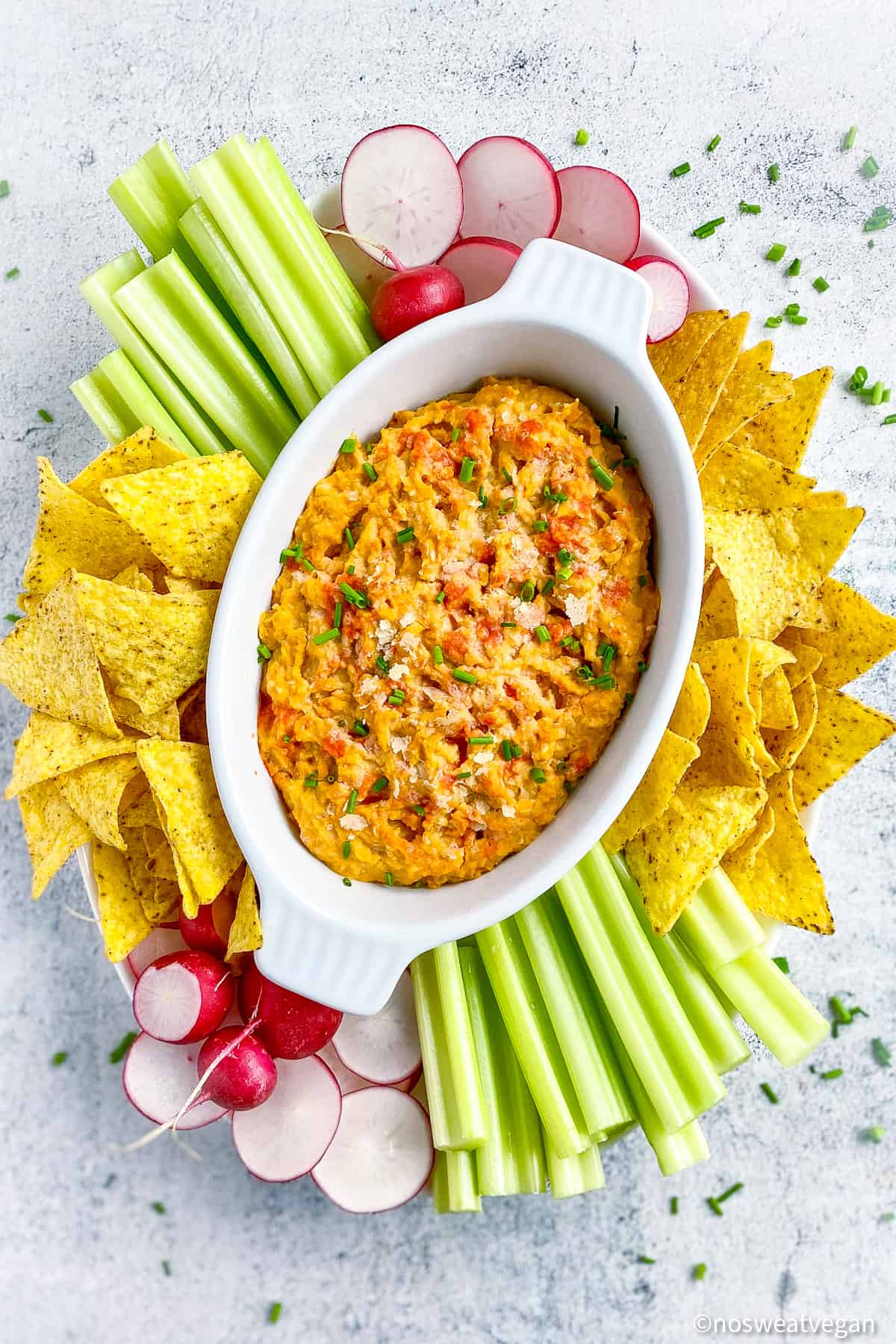 Buffalo chickpea dip on platter with chips, celery, and sliced radishes.