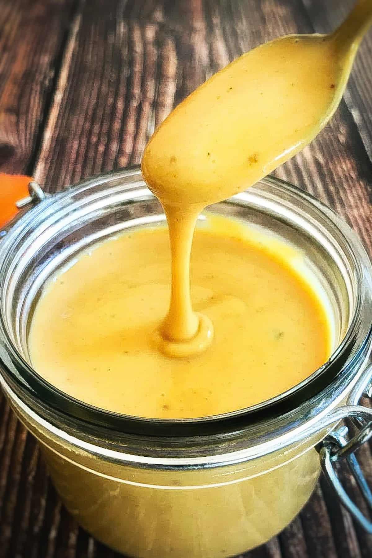 Vegan honey mustard dressing in a jar with spoon lifting up.