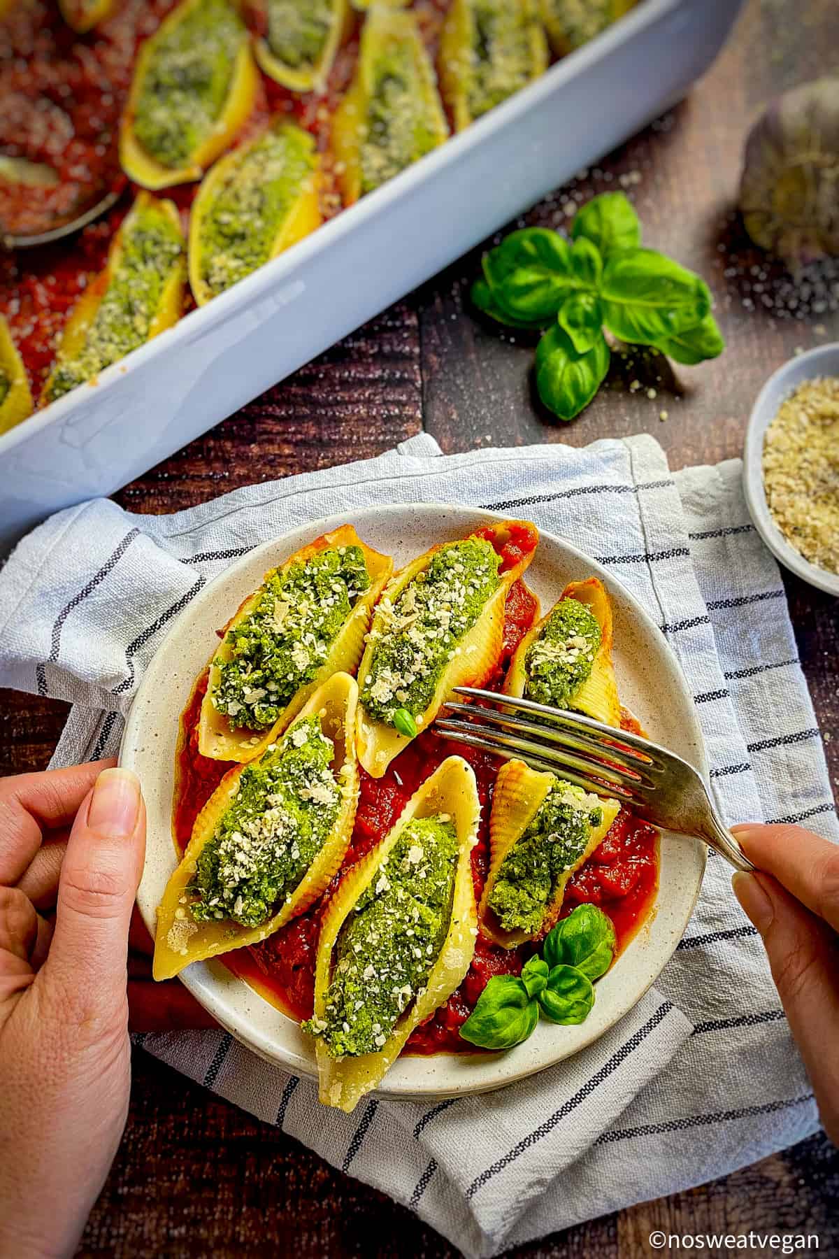 Vegan spinach and ricotta stuffed pasta shells on plate with fork cutting one in half.