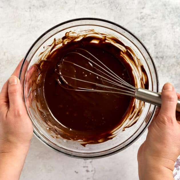 Two hands holding bowl with chocolate mixture and whisk.