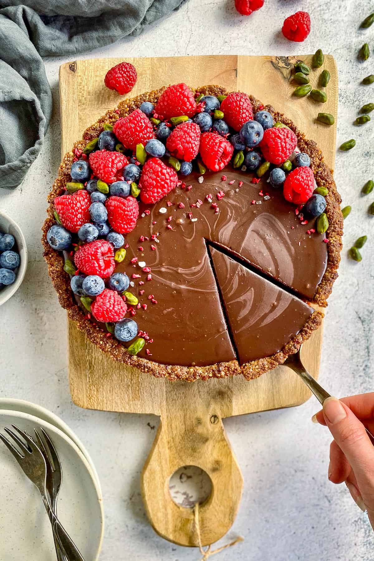 Vegan chocolate tart on a cutting board and topped with raspberries, blueberries, and pistachios.