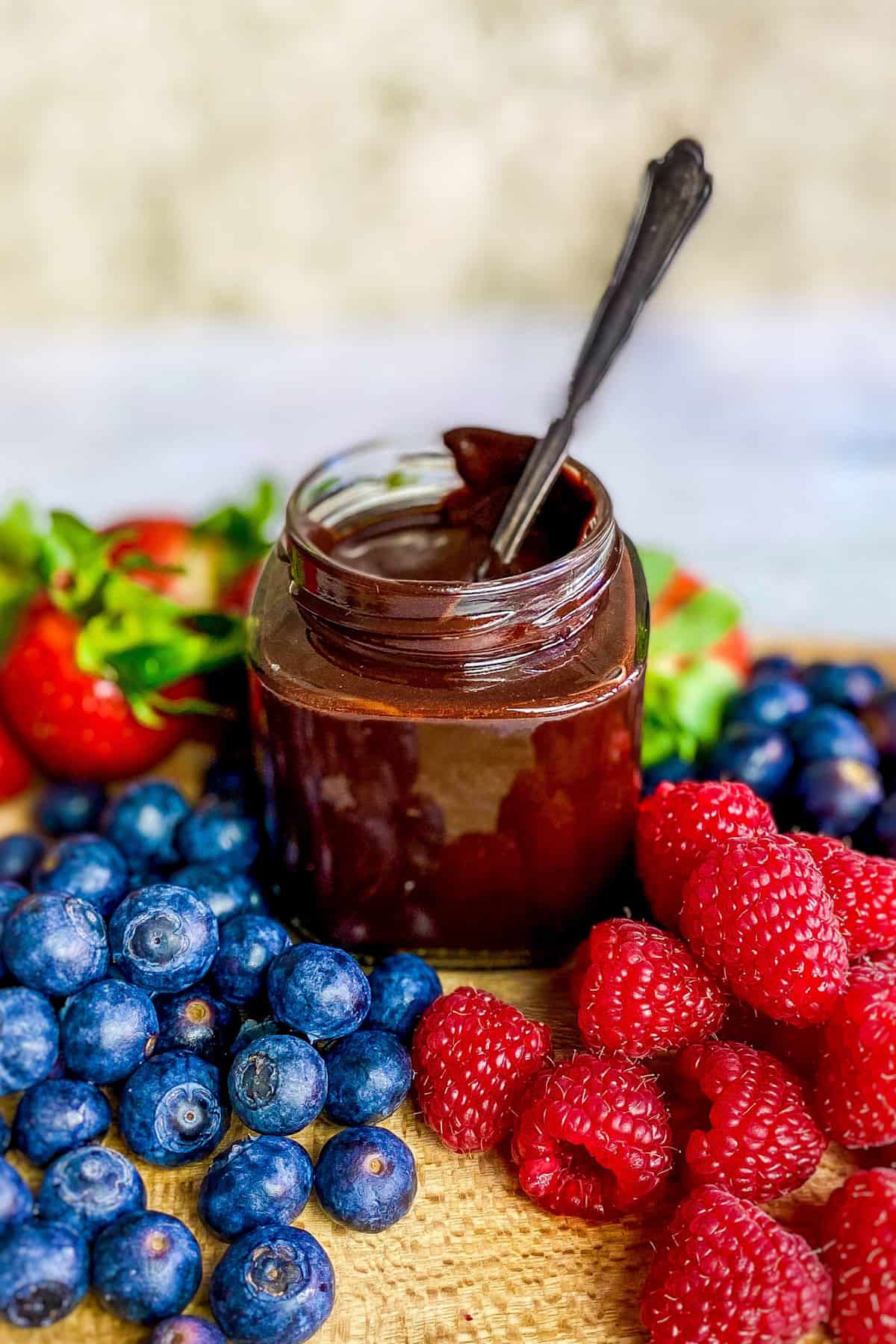 Vegan chocolate syrup in a jar surrounded by berries.