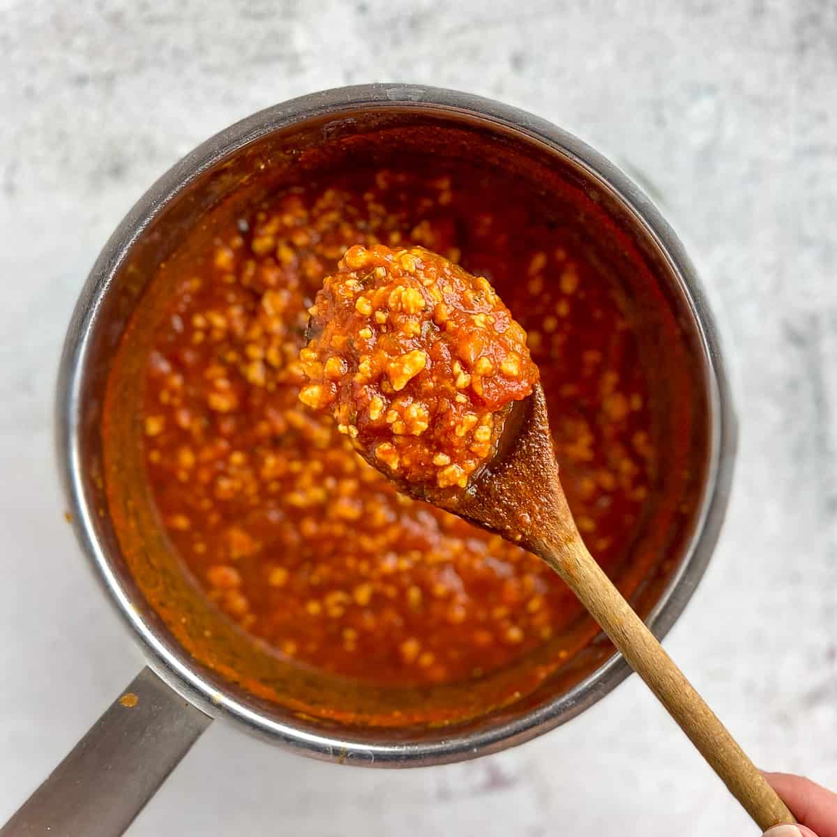Spoon lifting up vegan spaghetti sauce over a pot.