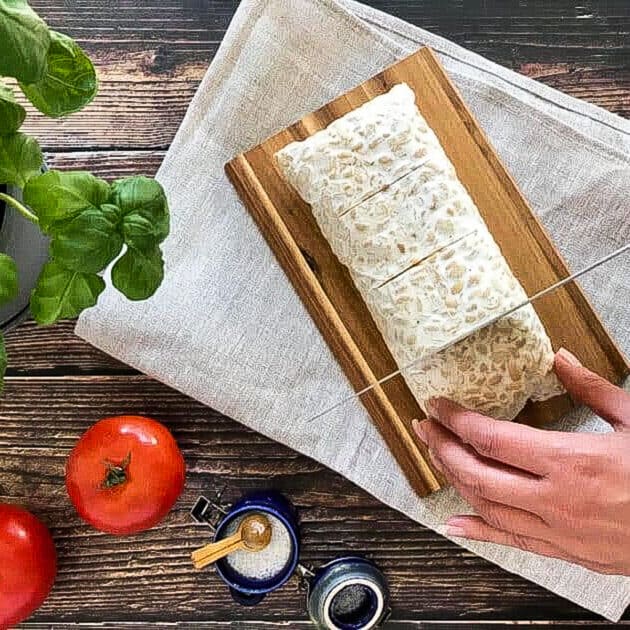 Hand slicing tempeh for vegan bacon.