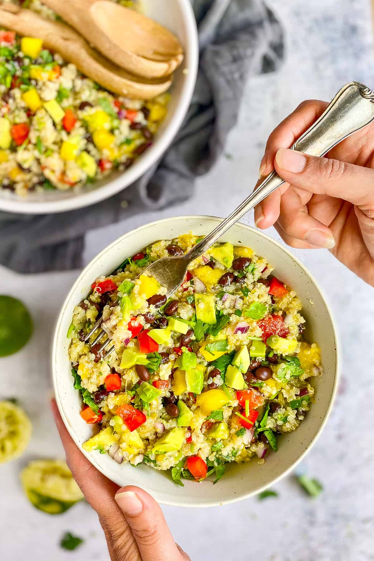 Hand holding a fork and a bowl of vegan quinoa salad.