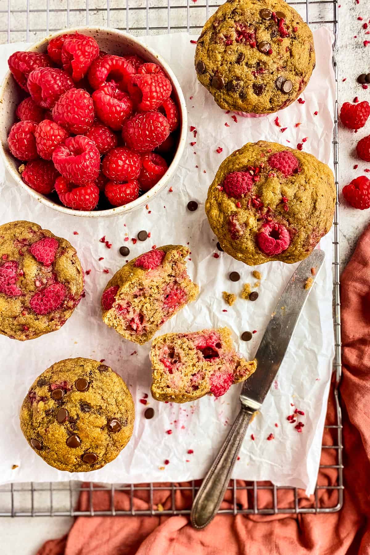 Raspberry muffins on a drying rack with a bowl of raspberries.