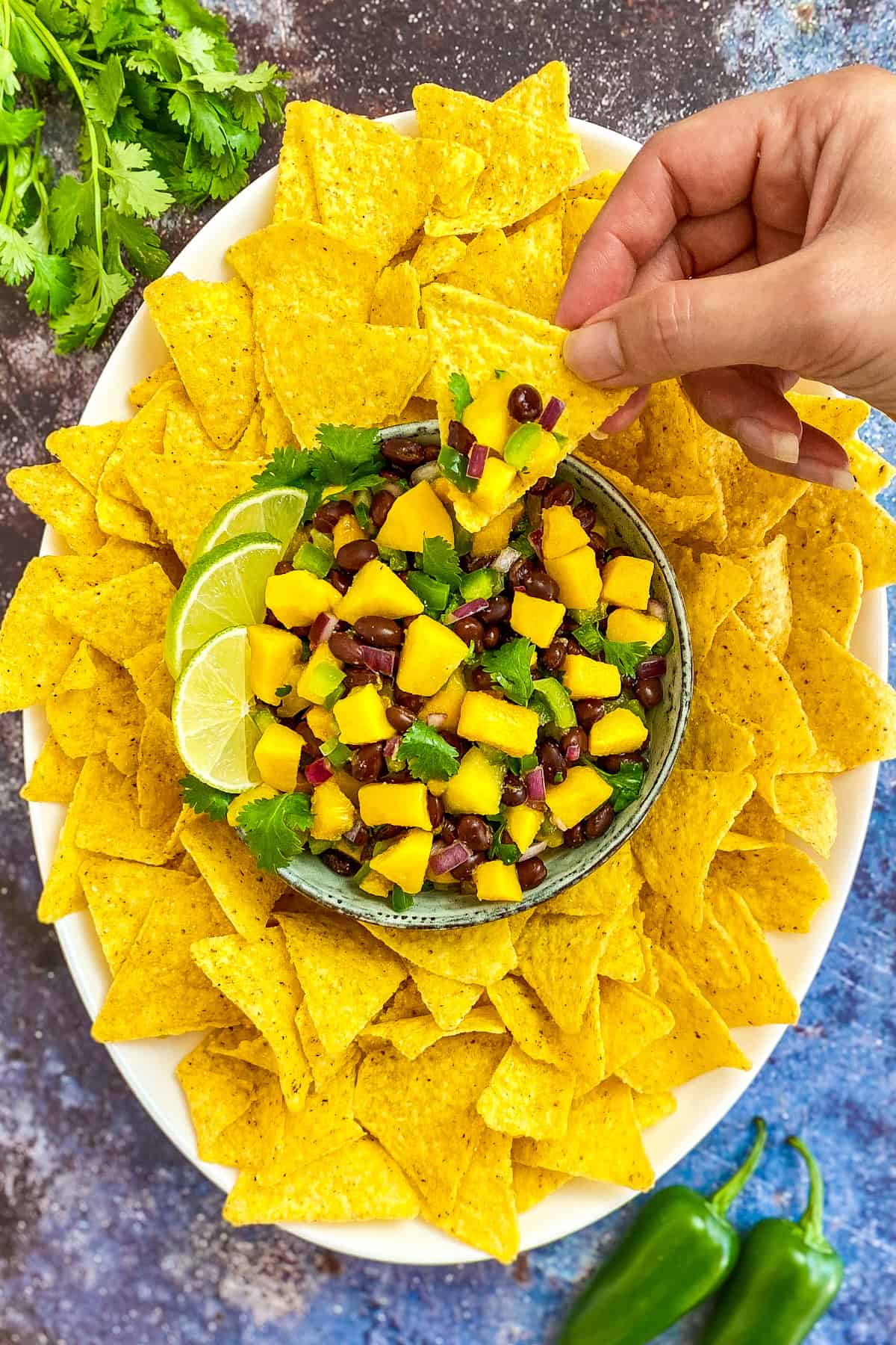 Mango and black bean salsa in bowl with chips and a hand dipping a chip into the salsa.