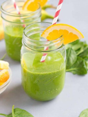 Spinach pineapple smoothies in jars with straws and orange slices.