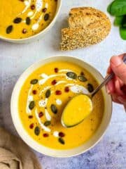 Butternut squash soup in a bowl with a hand lifting up a spoonful.