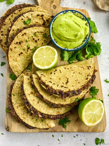 Vegan black bean tacos on a cutting board with avocado crema and limes.