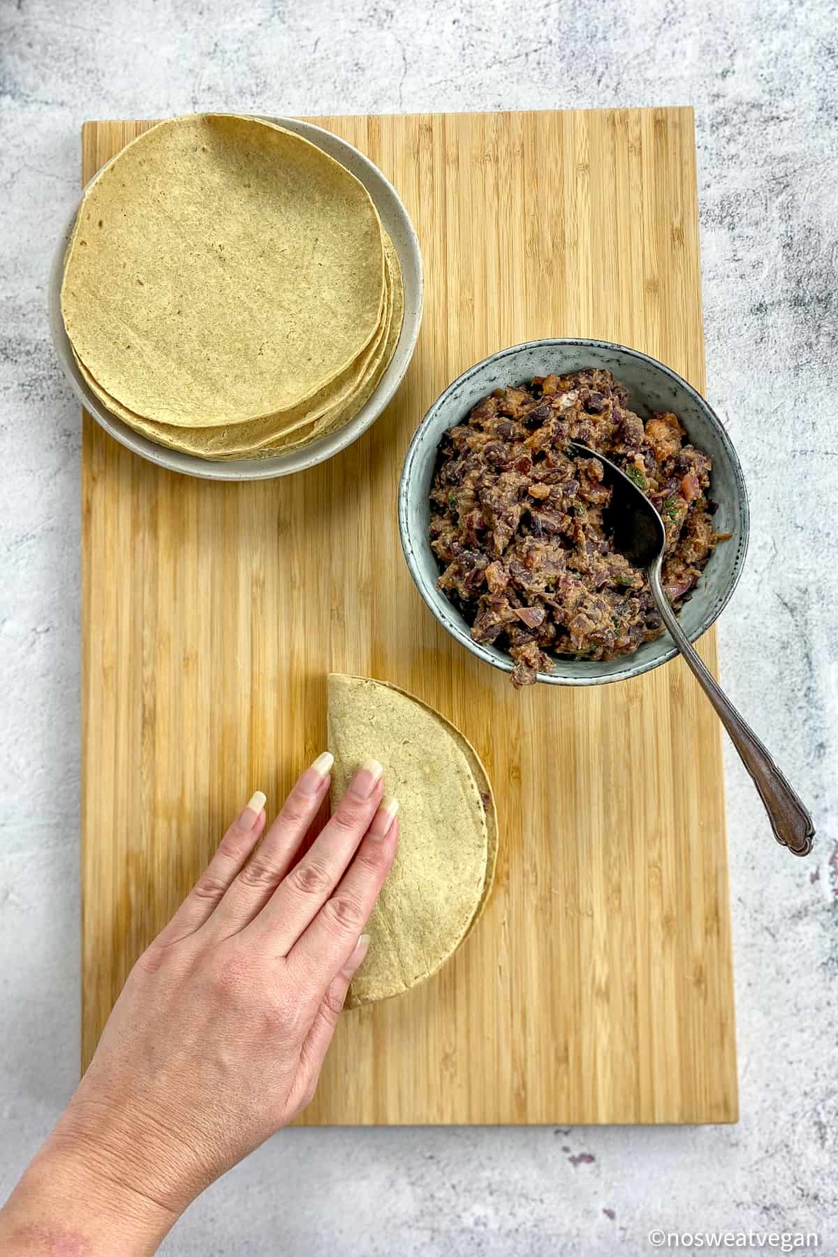Tortillas, bean mixture and a taco with a hand pressing it down.