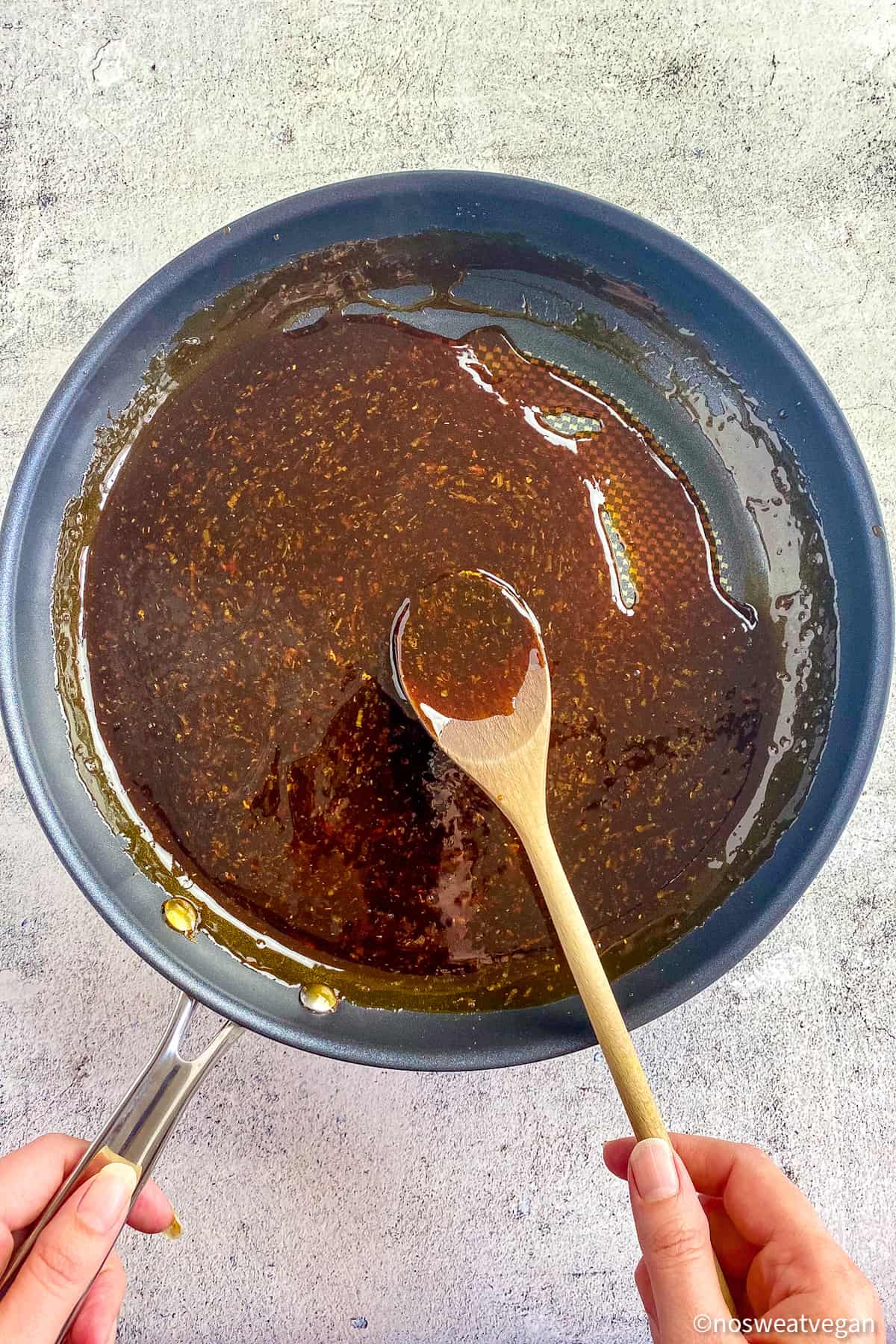 Teriyaki sauce in a skillet with a hand holding a wooden spoon.