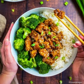 Bowl with teriyaki tofu, rice, and broccoli. Hand using chopsticks to pick up a chunk of tofu.