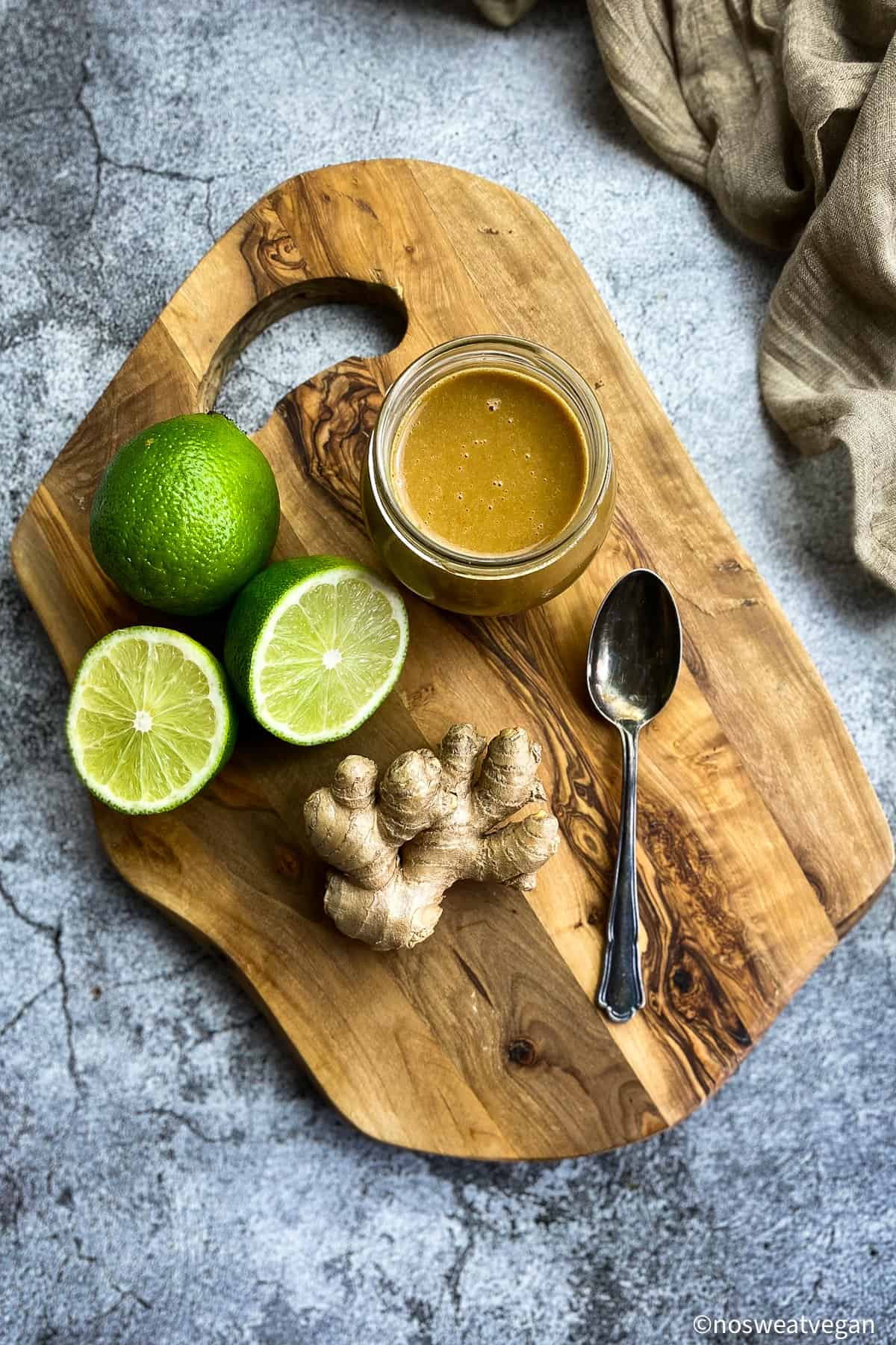 Tahini dressing on a cutting board with limes and ginger.