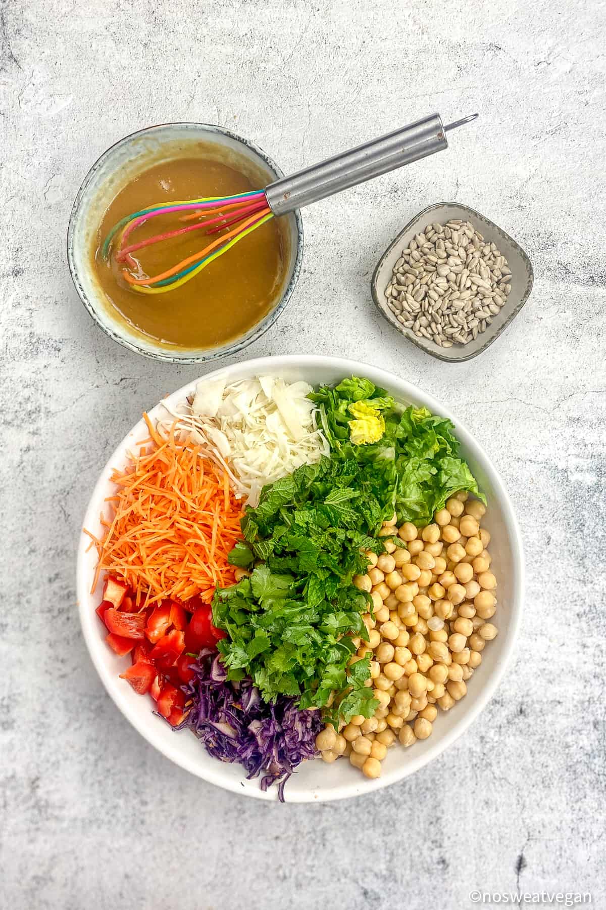 Rainbow salad in a bowl next to a smaller bowl of dressing and a bowl of sunflower seeds.