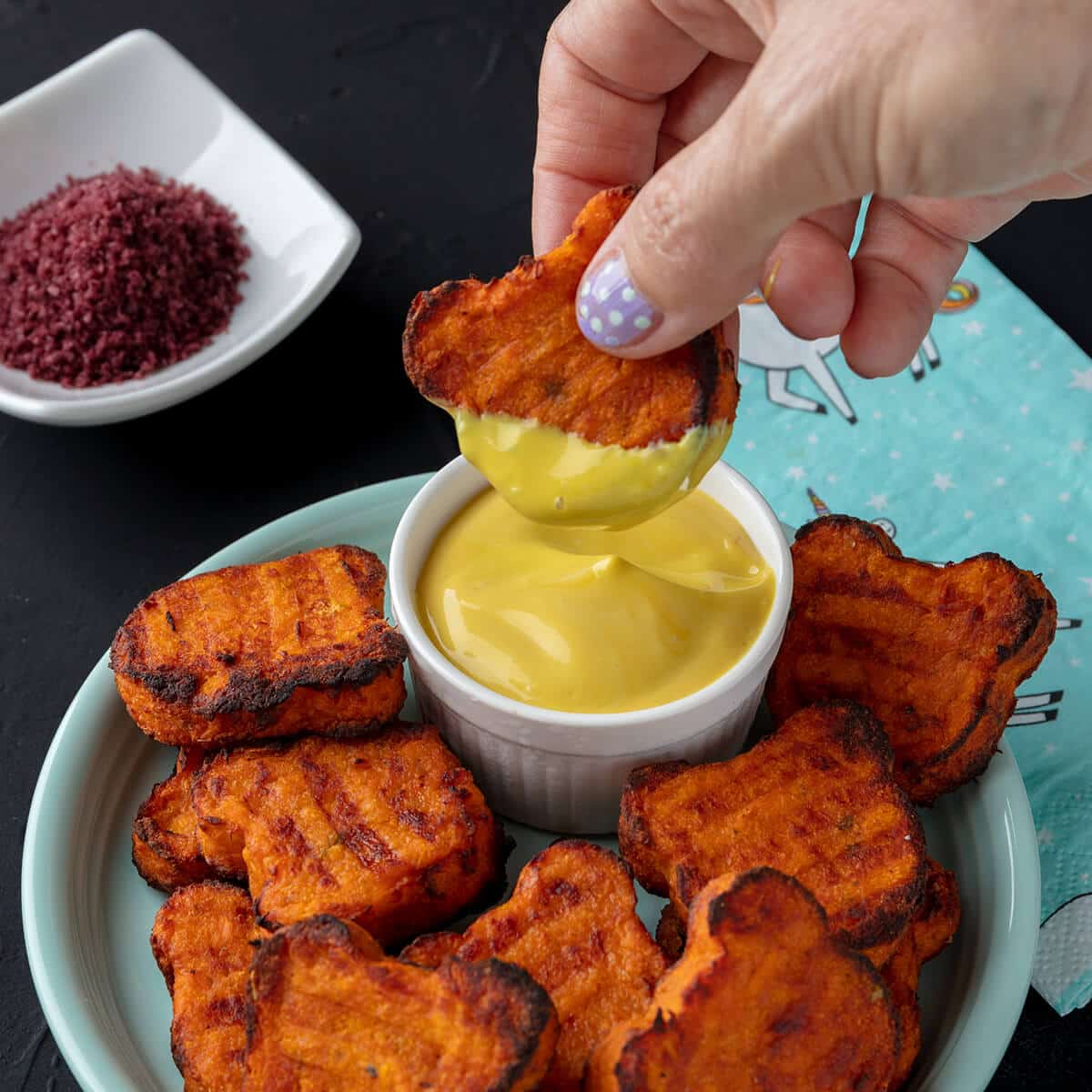 Hand dipping vegan sweet potato bites into dipping sauce.