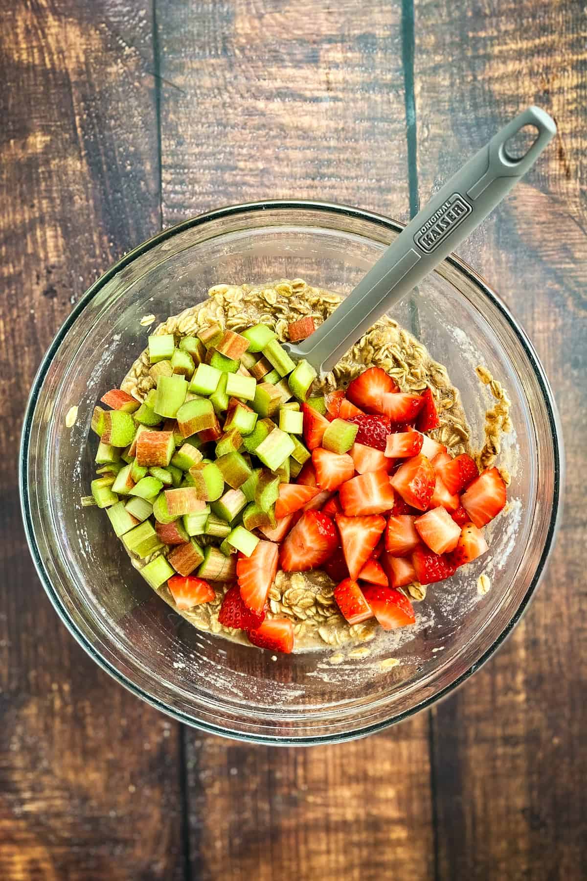 Rhubarb and strawberries added to an oatmeal mixture in a bowl.