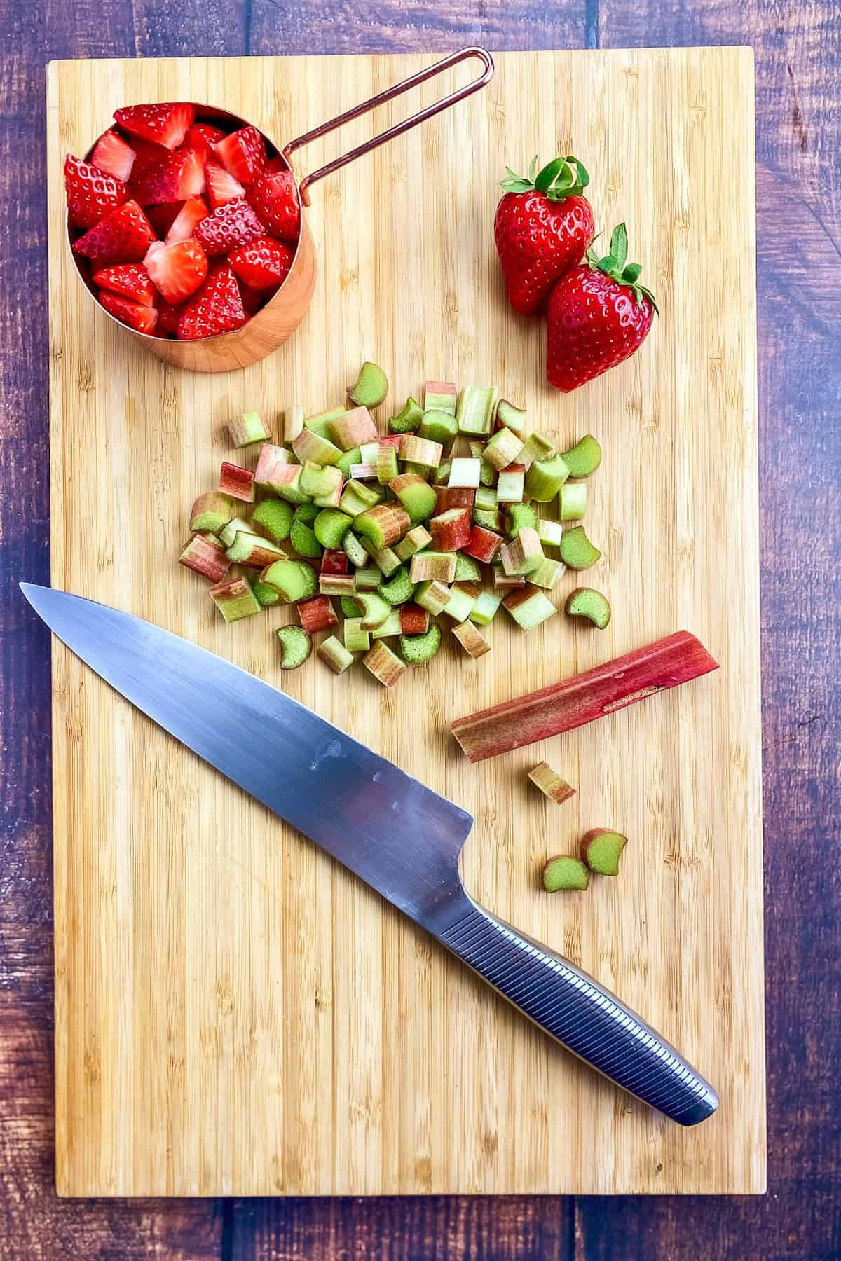 Cubed strawberries in a measuring cup and cubed rhubarb on a cutting board.