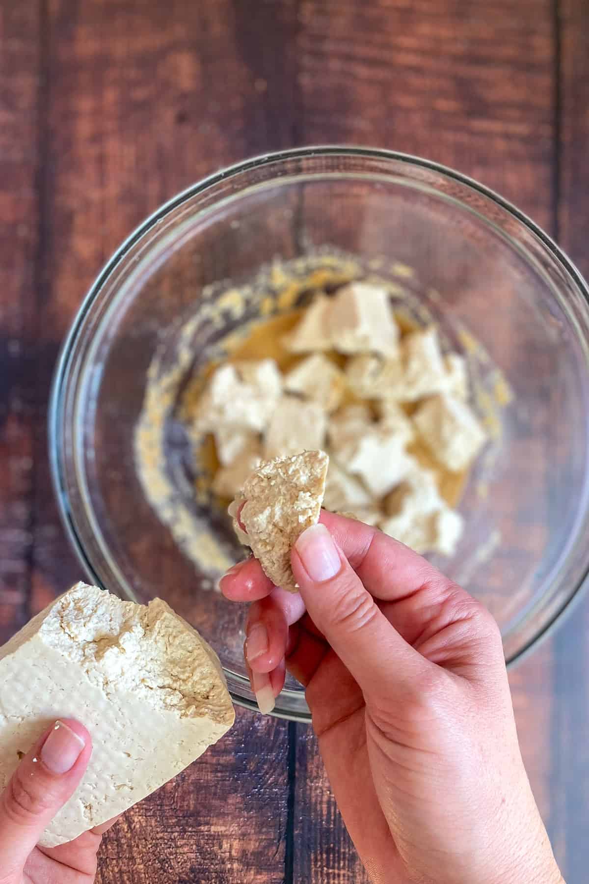 Two hands tearing tofu chunks over a bowl.